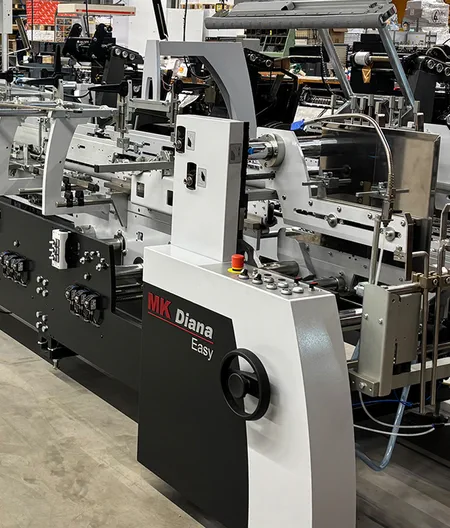 Industrielle Verpackungsmaschine Diana Easy 115 von MK im Einsatz bei X-Press zur Verarbeitung und Verklebung von Faltschachteln in der Produktionshalle von der Berliner Druckerei X-Press.